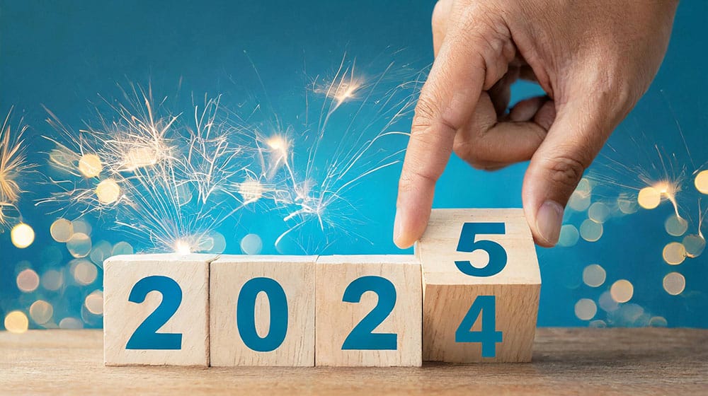 En hånd vender en træklods og ændrer året fra 2024 til 2025 med stjernekastere, der funkler klart i baggrunden, der symboliserer begyndelsen af FutureNode.dk's innovative vision for i morgen.