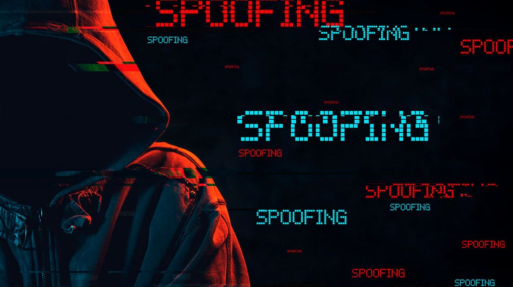 En person i en jakke med hætte står i skygge, omgivet af ordet "SPOOFING" i glitch-stil - et visuelt nik til risikoen ved spoofing og et spørgsmål: Hvad er spoofing?.