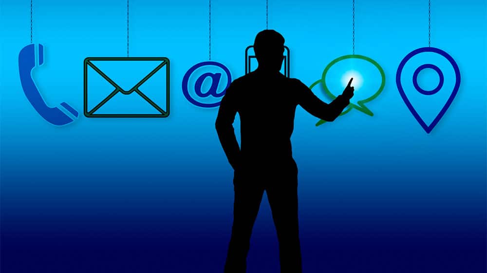 Silhuet af en person, der rører ved et lysende chat-ikon, med telefon-, e-mail-, Outlook-, Proton-, Gmail-, at-symbol-, chat- og placeringsikoner hængende i en række på en blå baggrund.
