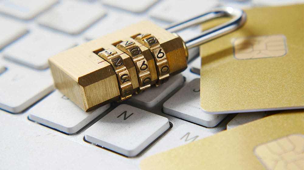 En kombinationshængelås, et guldkreditkort og et SIM-kort ligger på et computertastatur, hvilket antyder digital sikkerhed og privatliv på nettet – og understreger vigtigheden af at bruge en adgangskodemanager for at træffe det bedste valg inden for sikkerhed.
